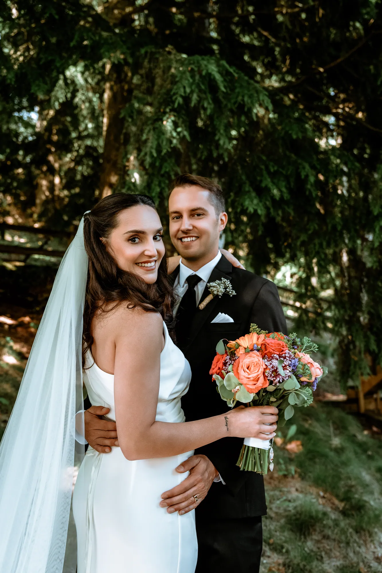 A bride and groom standing together in the forest, the bride holding a bright autumn bouquet