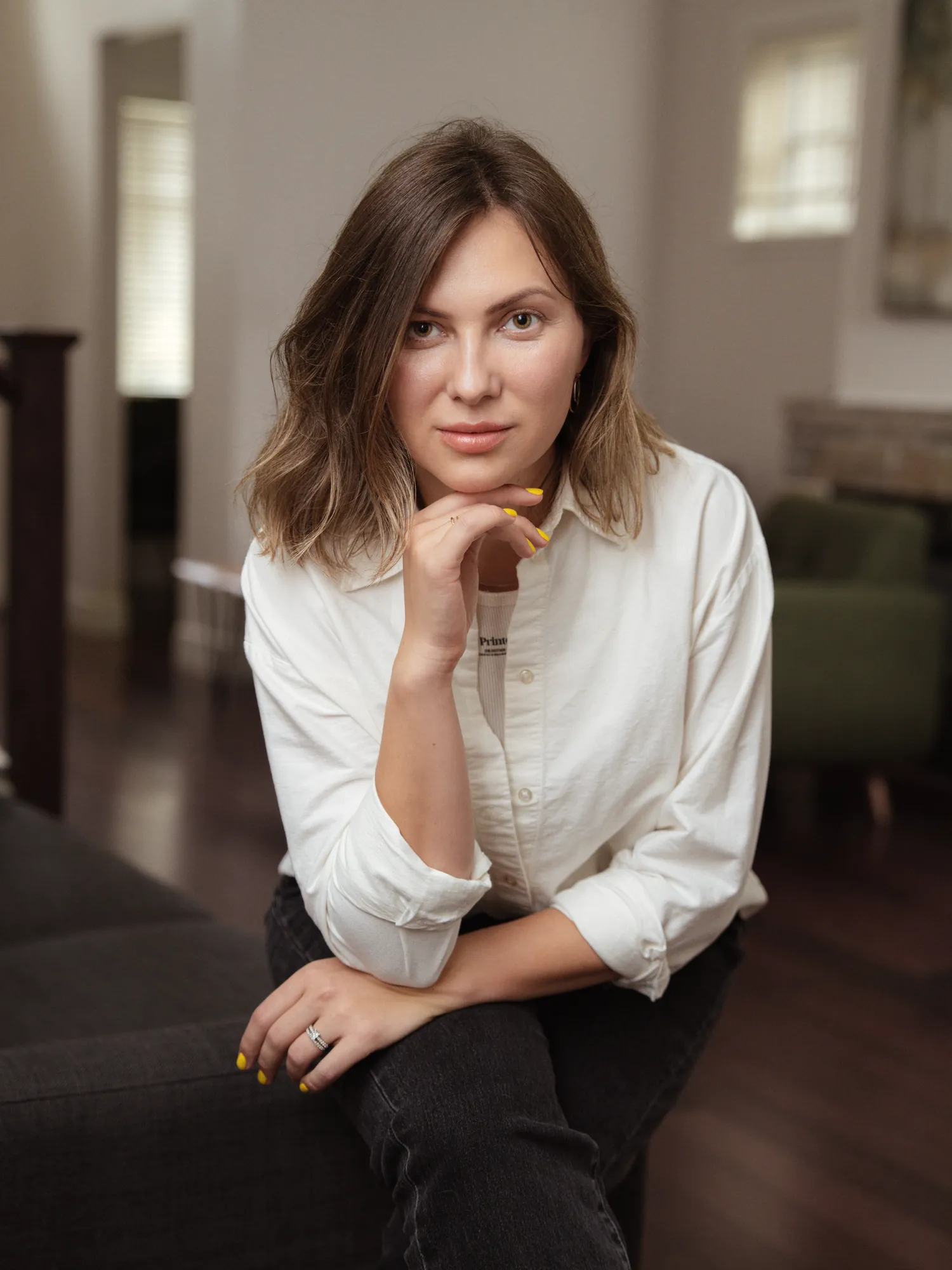 Portrait of Ivanna seated indoors in a white shirt, resting her chin on her hand