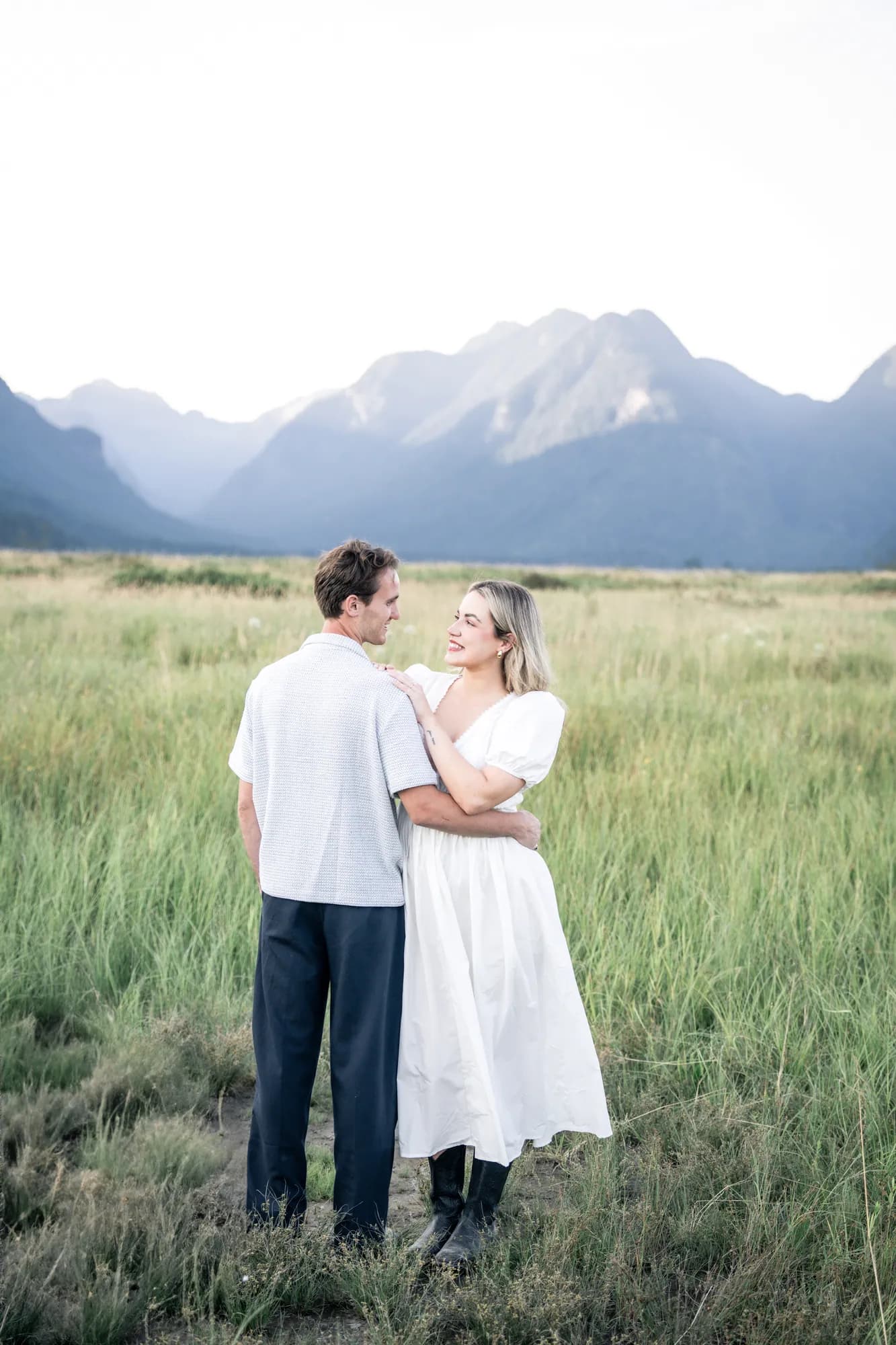 A couple embracing in a wide grass field with mountains rising behind them