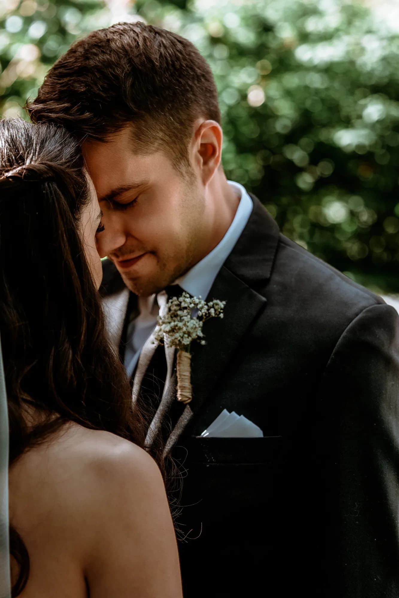 A groom resting his forehead against his bride's shoulder, eyes closed