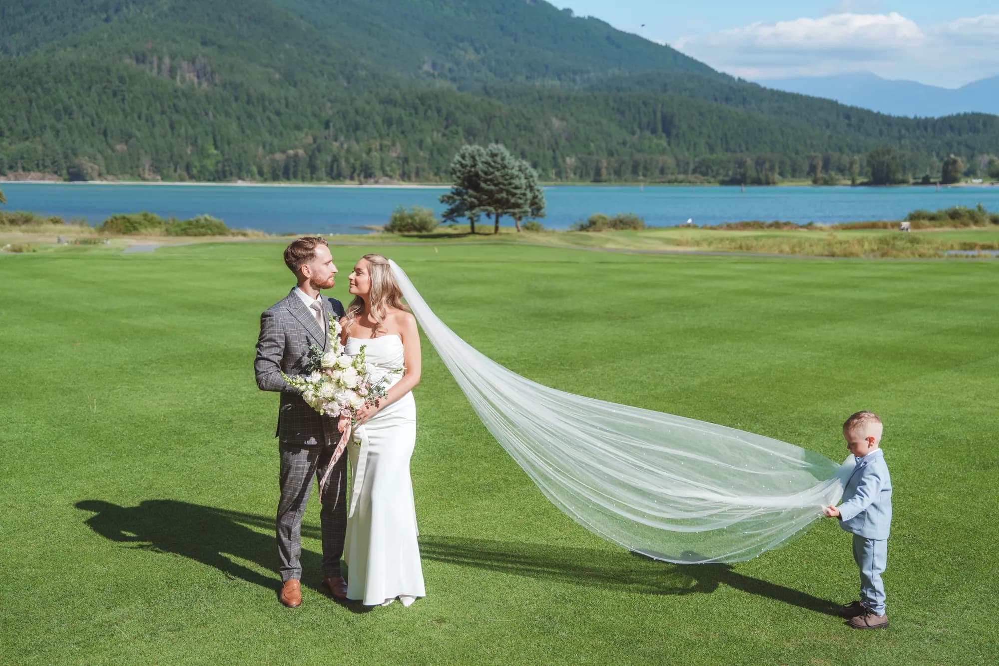 A bride's long veil sweeping across a lawn with the lake and mountains beyond