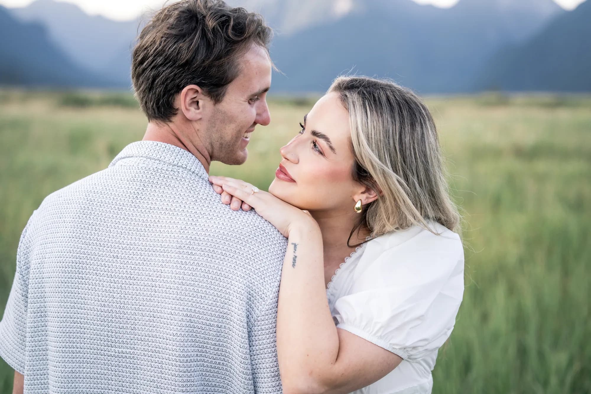 A couple holding each other in a tall grass field, mountains behind them