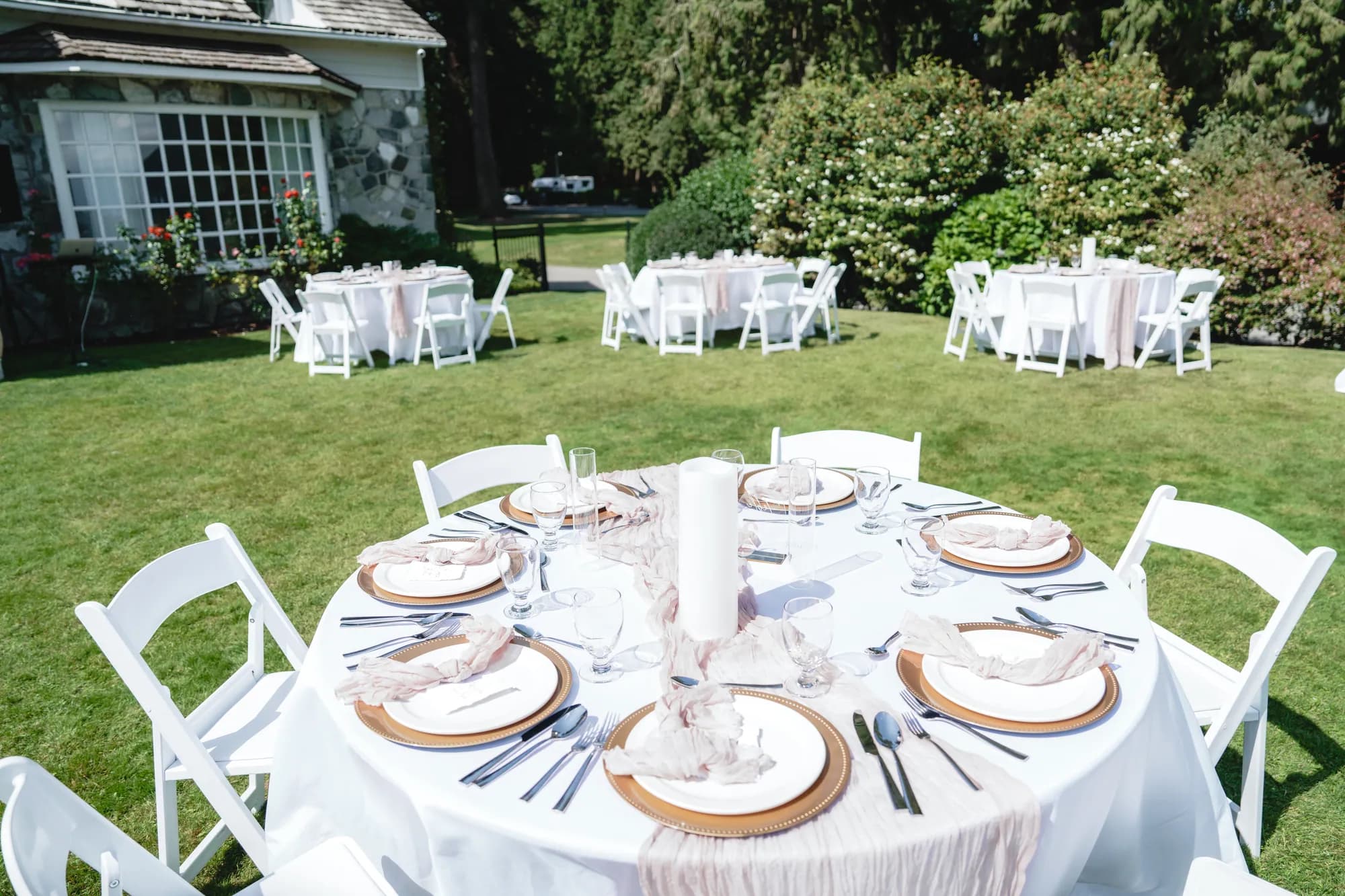 A round reception table set with linen, candles and glassware on a lawn